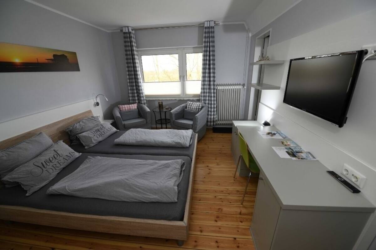 A bedroom with a bed, two armchairs, a small table, a TV, and a window with curtains.