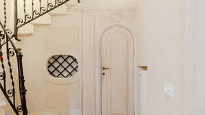 A staircase with ornate black balusters leading to a white door with a decorative keyhole and a circular window. - Residenza Del Cedro (Rome)
