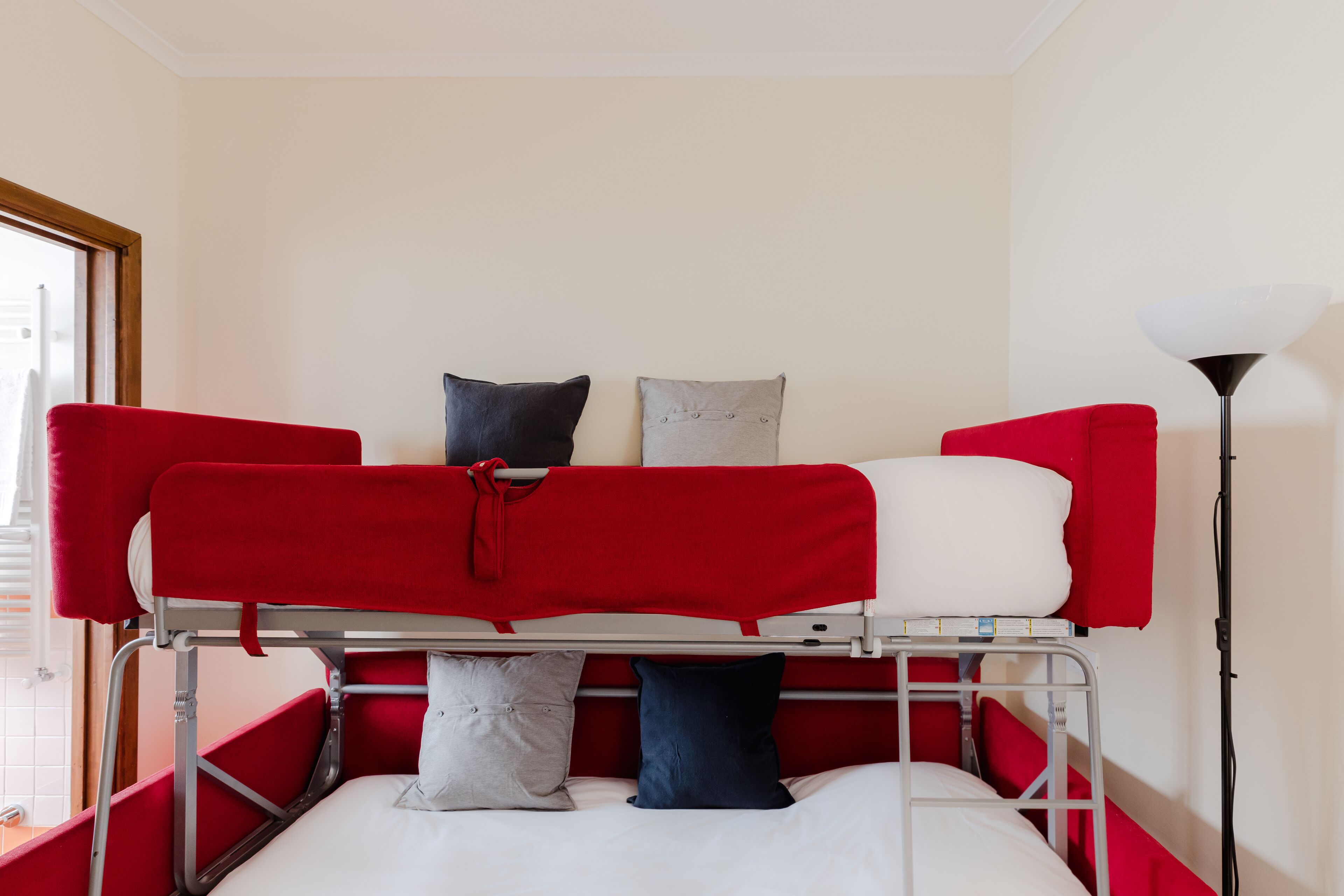 Un lit superposé avec une literie rouge et blanche, un oreiller gris et un oreiller bleu.