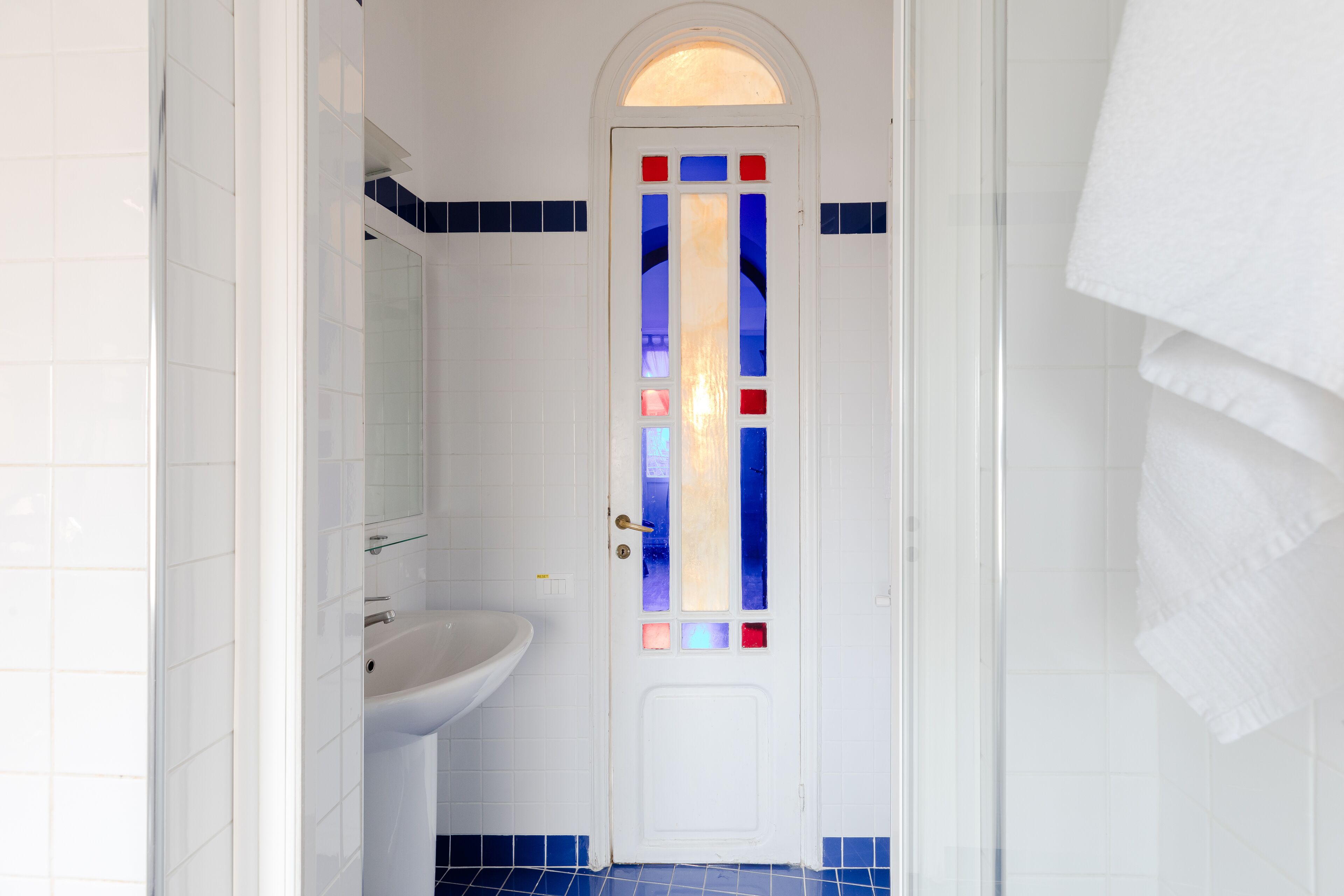 A bathroom with a white sink, a door with stained glass, and blue-tiled walls.