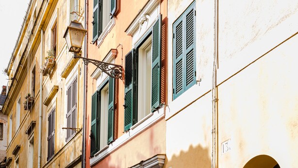 A cobblestone street with buildings featuring arched doorways and green shutters. - Residenza Del Cedro (Rome)