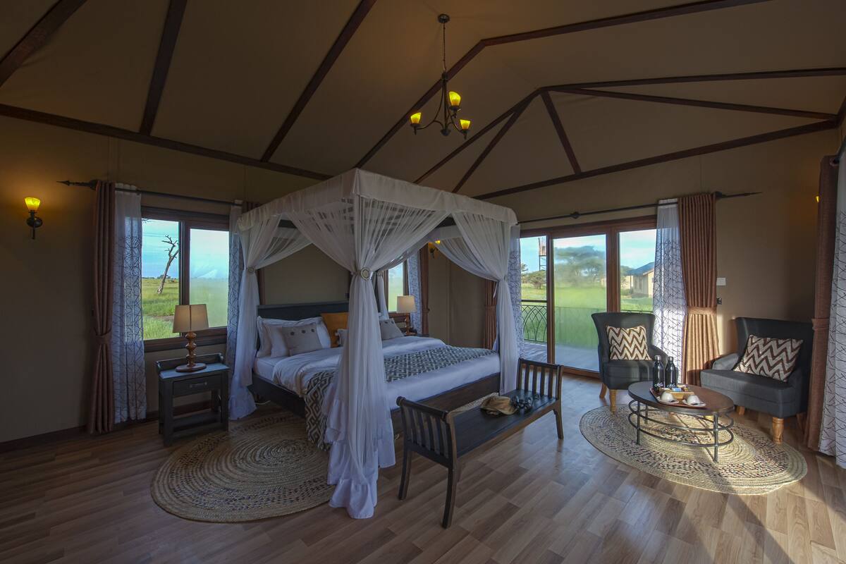 A spacious bedroom with a four-poster bed, a sitting area with a round table, and a view of the outdoors.