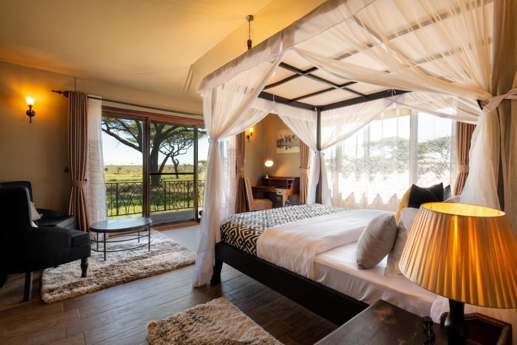 A bedroom with a bed, bedside table, lamp, and a view of the outdoors.