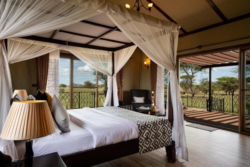 A bedroom with a canopy bed, a bedside lamp, a chair, and a view of the outdoors.