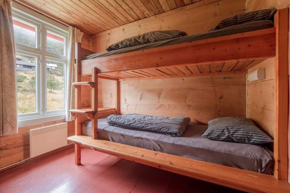 A bunk bed room with a window, wooden walls, and a radiator.