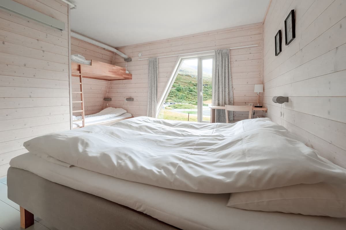 A bedroom with a bunk bed, a desk, and a window with curtains.