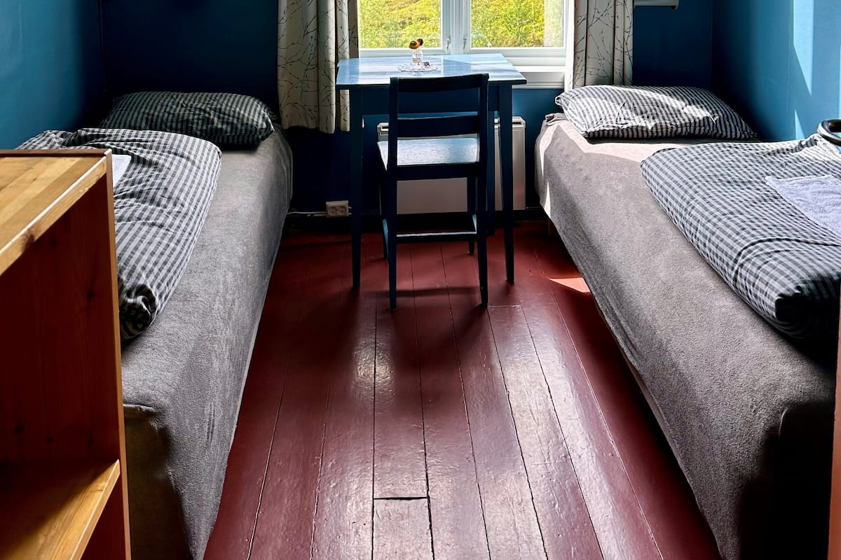 A dormitory room with two beds, a wooden desk, and a window with curtains.