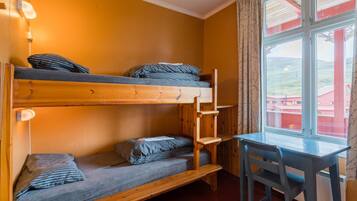A bunk bed room with a desk and chair, a window with a view, and a lamp on the wall.