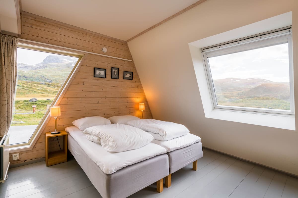 A bedroom with a bed, two bedside lamps, a window, and a view of the outdoors.