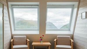 Habitación con dos ventanas y vistas a la montaña, una mesita con un florero y dos sillas.