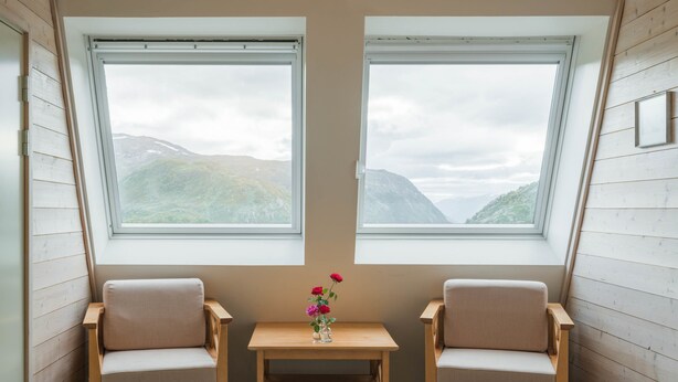 Habitación con dos ventanas y vistas a la montaña, una mesita con un florero y dos sillas.