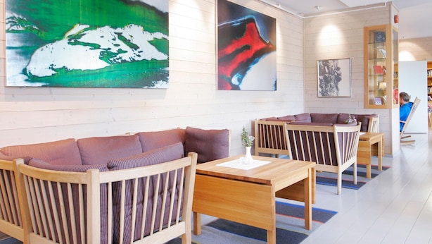 A modern hotel lobby with wooden furniture, large abstract paintings, and a bookshelf. - Turtagrø Hotel (Luster)