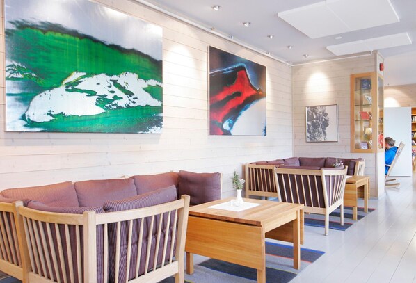 Un moderno vestíbulo de hotel con muebles de madera, grandes cuadros abstractos y una estantería.