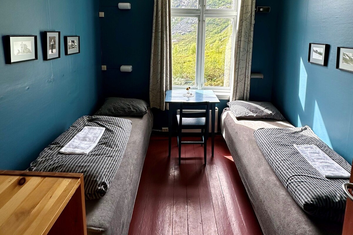 A room with two single beds, a small table, and a window with a view of greenery.