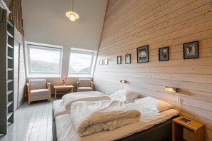 A bedroom with two beds, a wooden sloped ceiling, a window, and a wall with framed pictures. - Turtagrø Hotel (Luster)