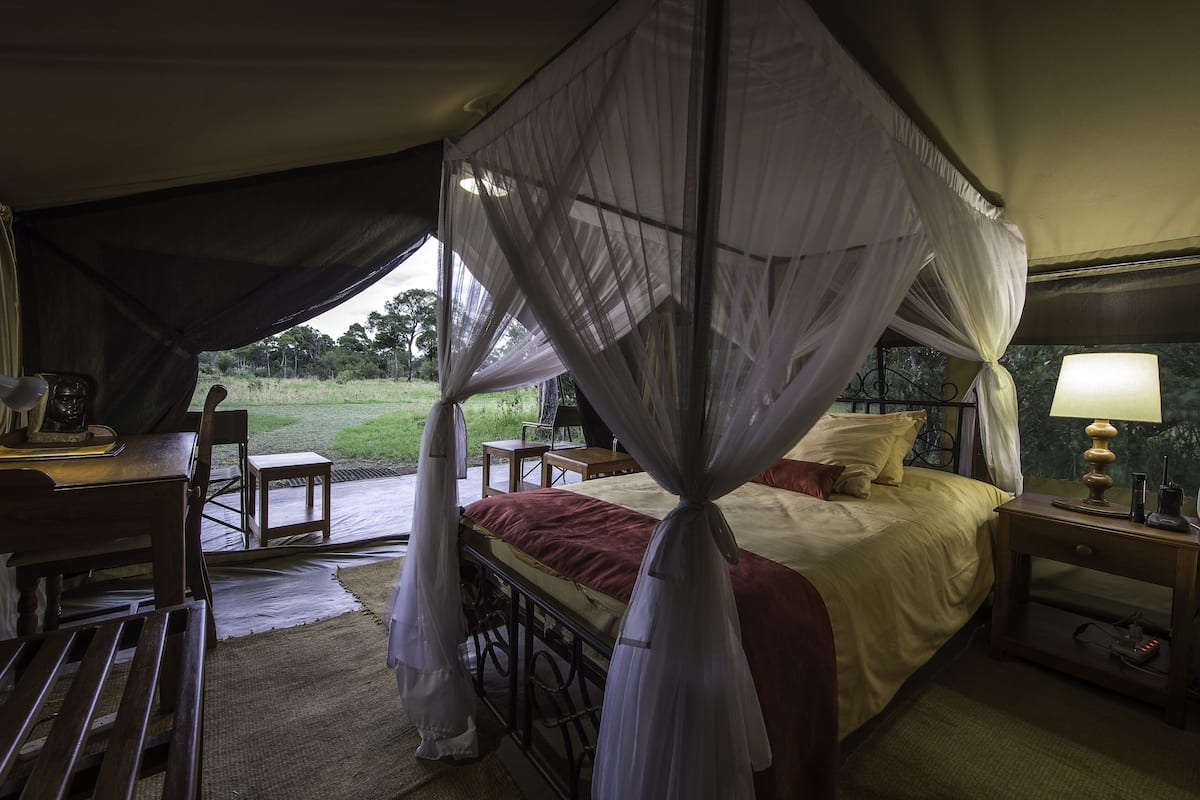 A room with a bed, a desk, and a chair. There is a canopy over the bed.