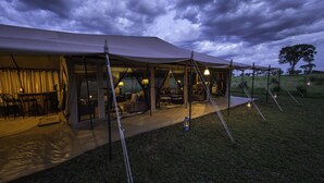 Un hébergement sous tente doté d’un espace extérieur couvert avec des sièges et d’un éclairage intérieur.