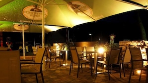 An outdoor dining area with tables and chairs under umbrellas, a stone wall, and a sign with German text. - Landgasthof Rebstock (Ottenhofen im Schwarzwald)