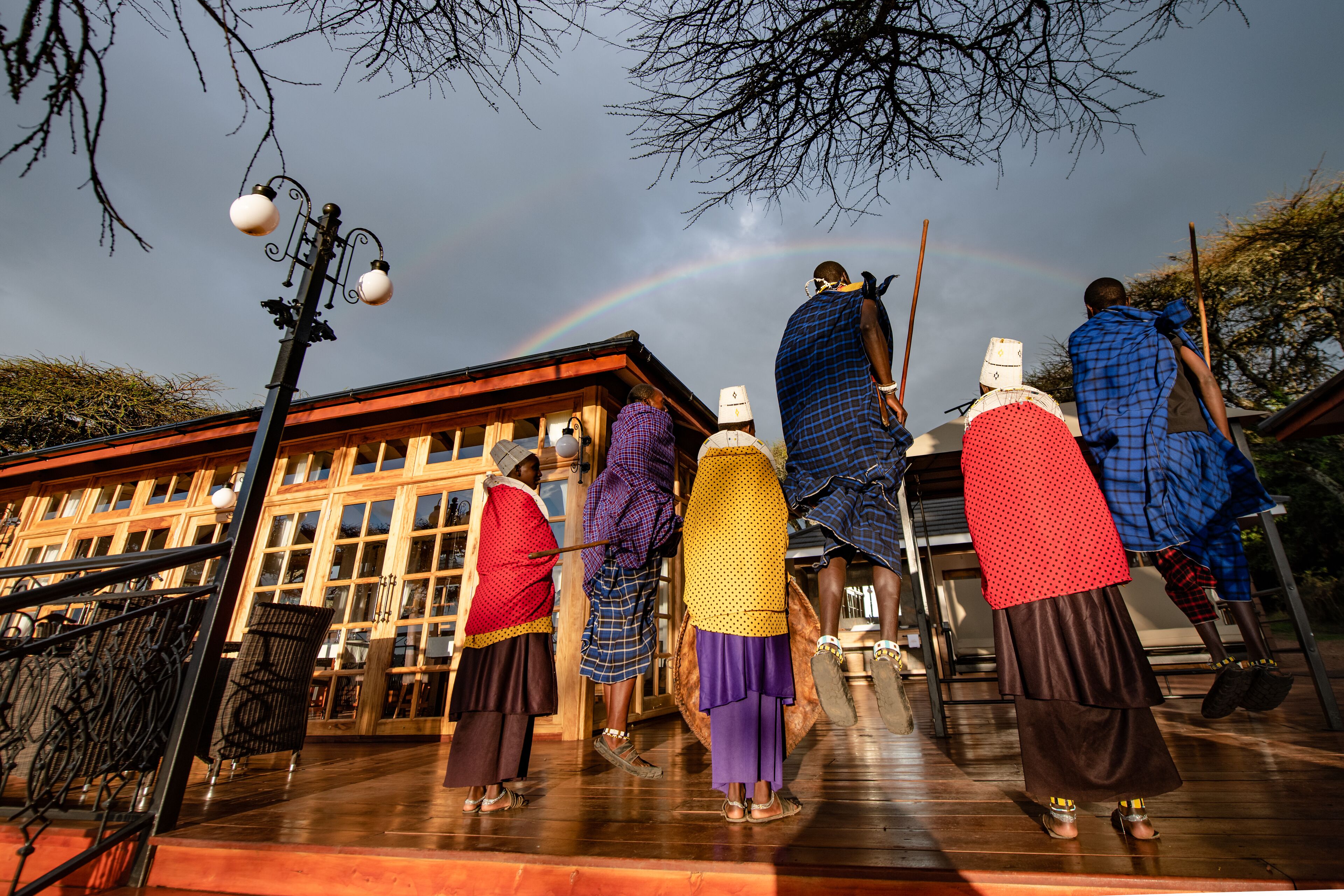 A group of people in traditional attire standing on a wooden deck with a building in the background.