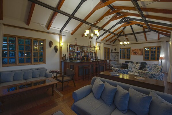 A spacious living area with a high ceiling, wooden beams, a bar, and seating arrangements. - Ngorongoro Lions Paw (Ngorongoro)