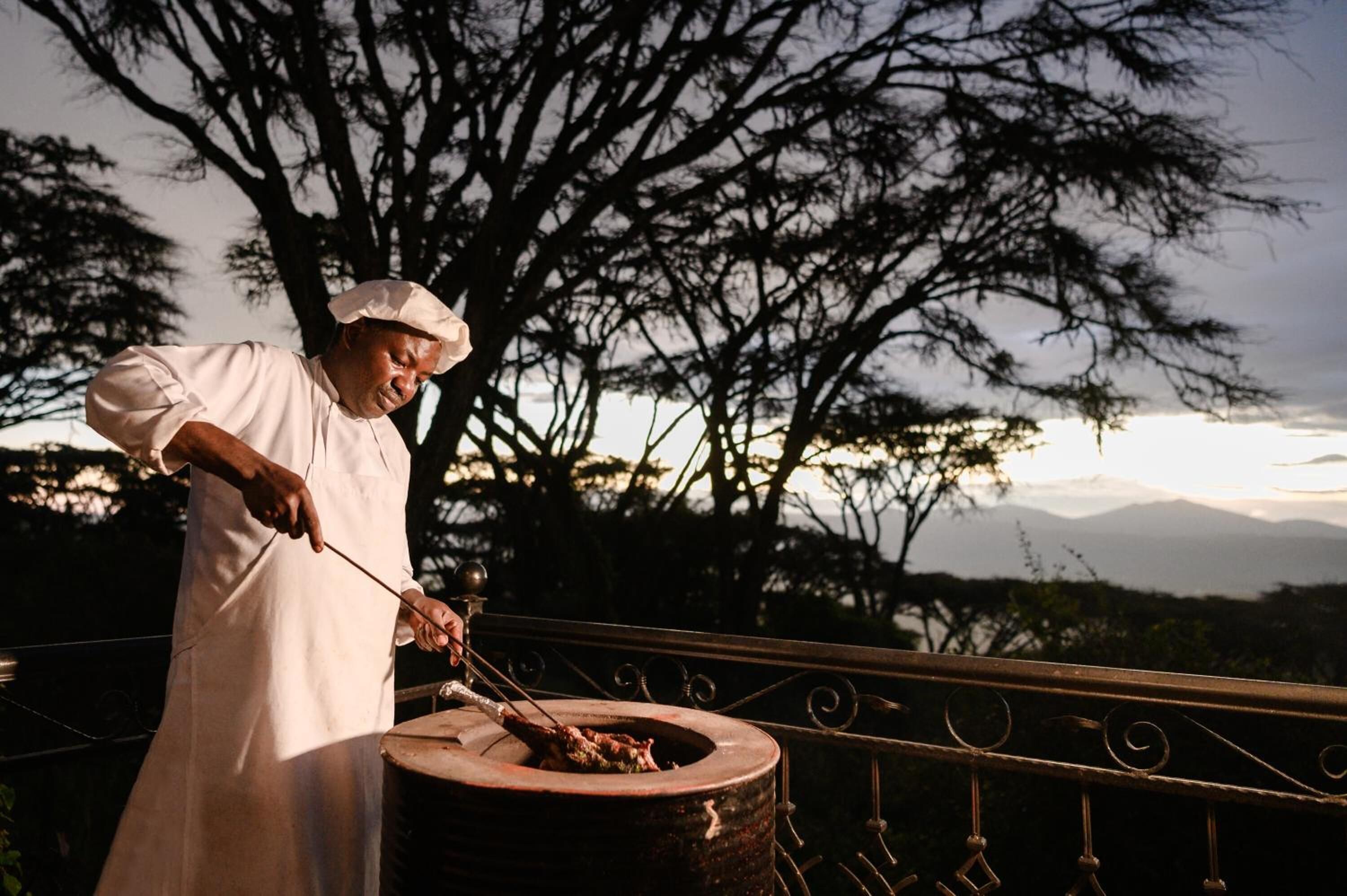 Un chef asando al aire libre con un hermoso paisaje de montañas.