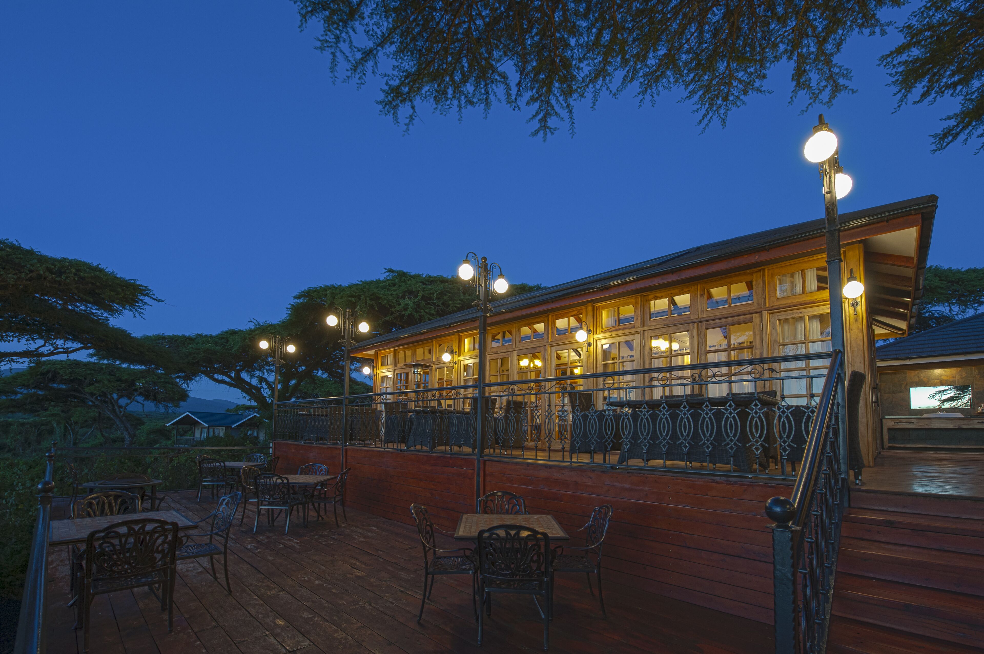 A wooden deck with outdoor seating and a railing, overlooking a building with multiple windows and a balcony.