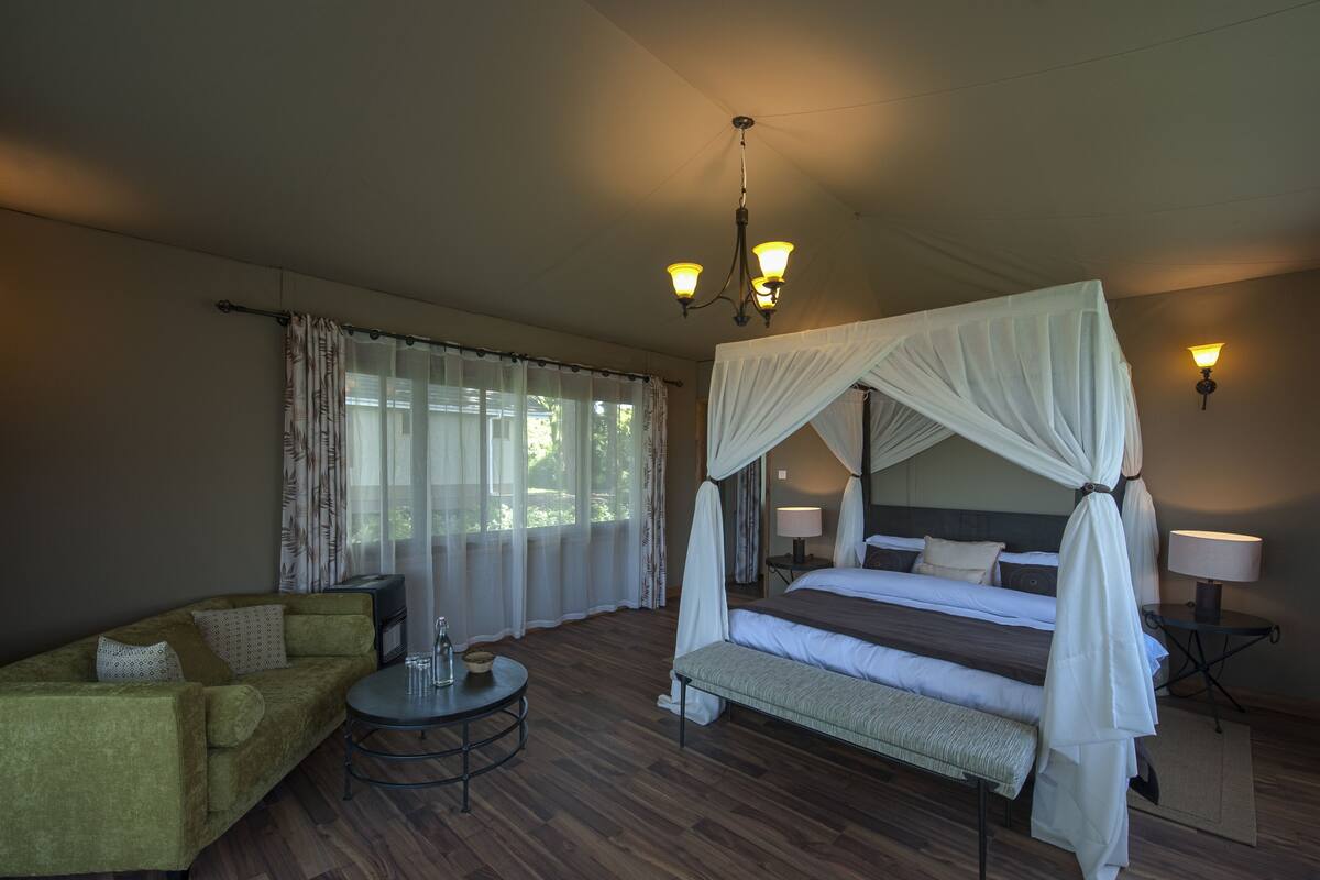 A hotel room with a four-poster bed, a sofa, a small round table, and a bedside lamp.