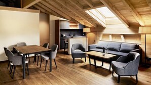 A modern loft-style room with a wooden ceiling, a dining area with a table and chairs, a sofa, and a kitchen area with a countertop and cabinets. - Hotel Alpenland (Lauenen)