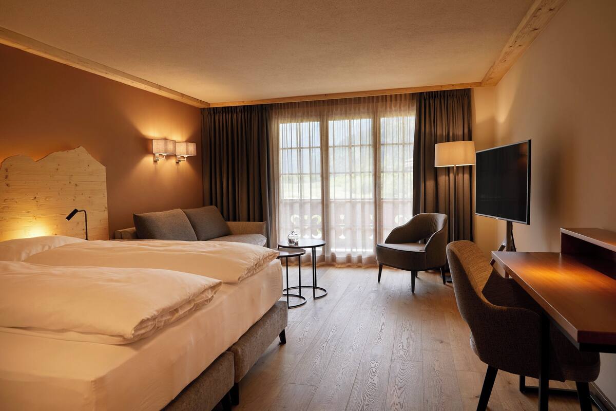 A hotel room with two beds, a desk, a chair, a TV, and a small table.