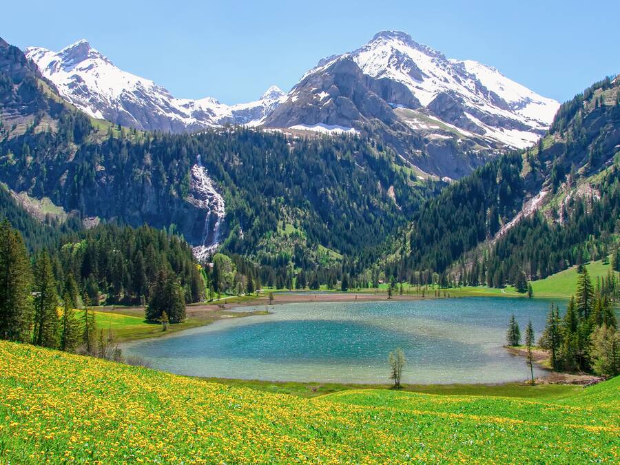 Un paisaje montañoso con un lago, zonas boscosas y picos nevados.
