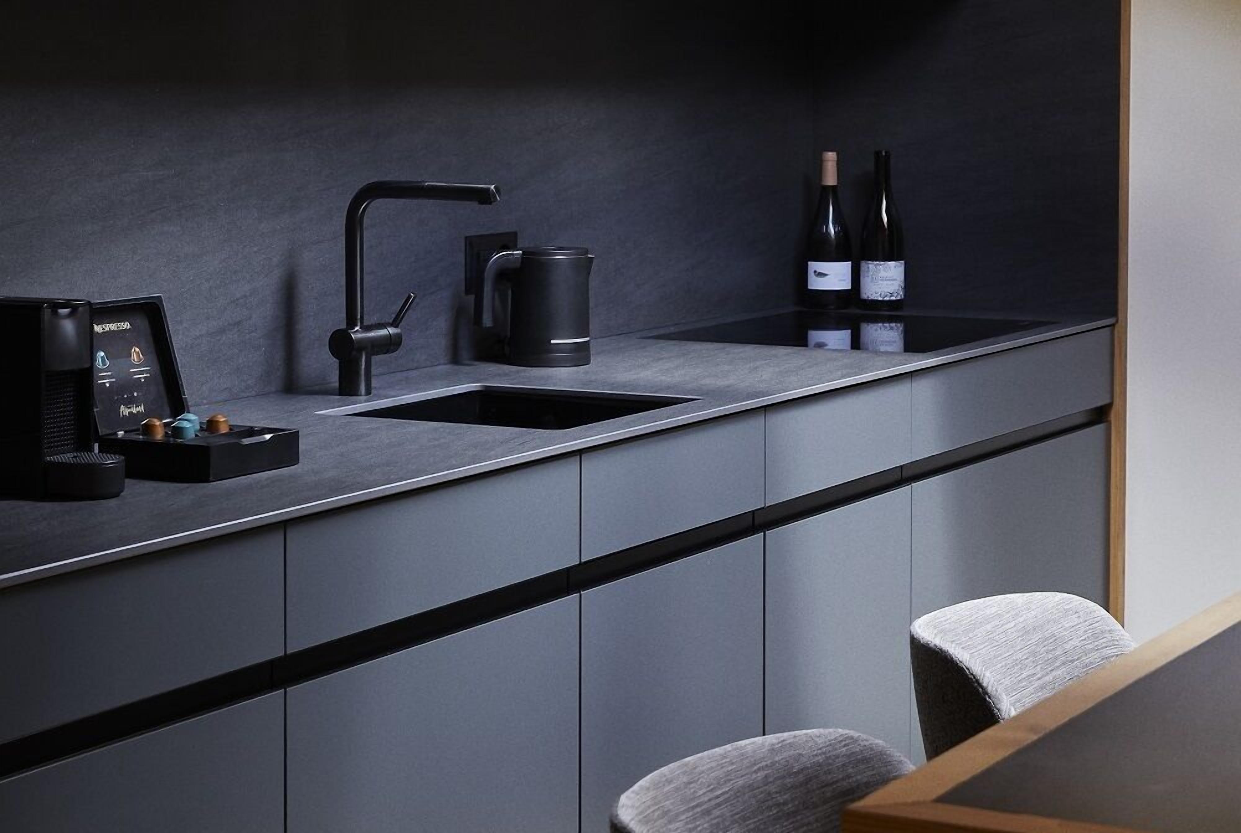 A modern kitchen with a black countertop, a coffee machine, a kettle, and two wine bottles.