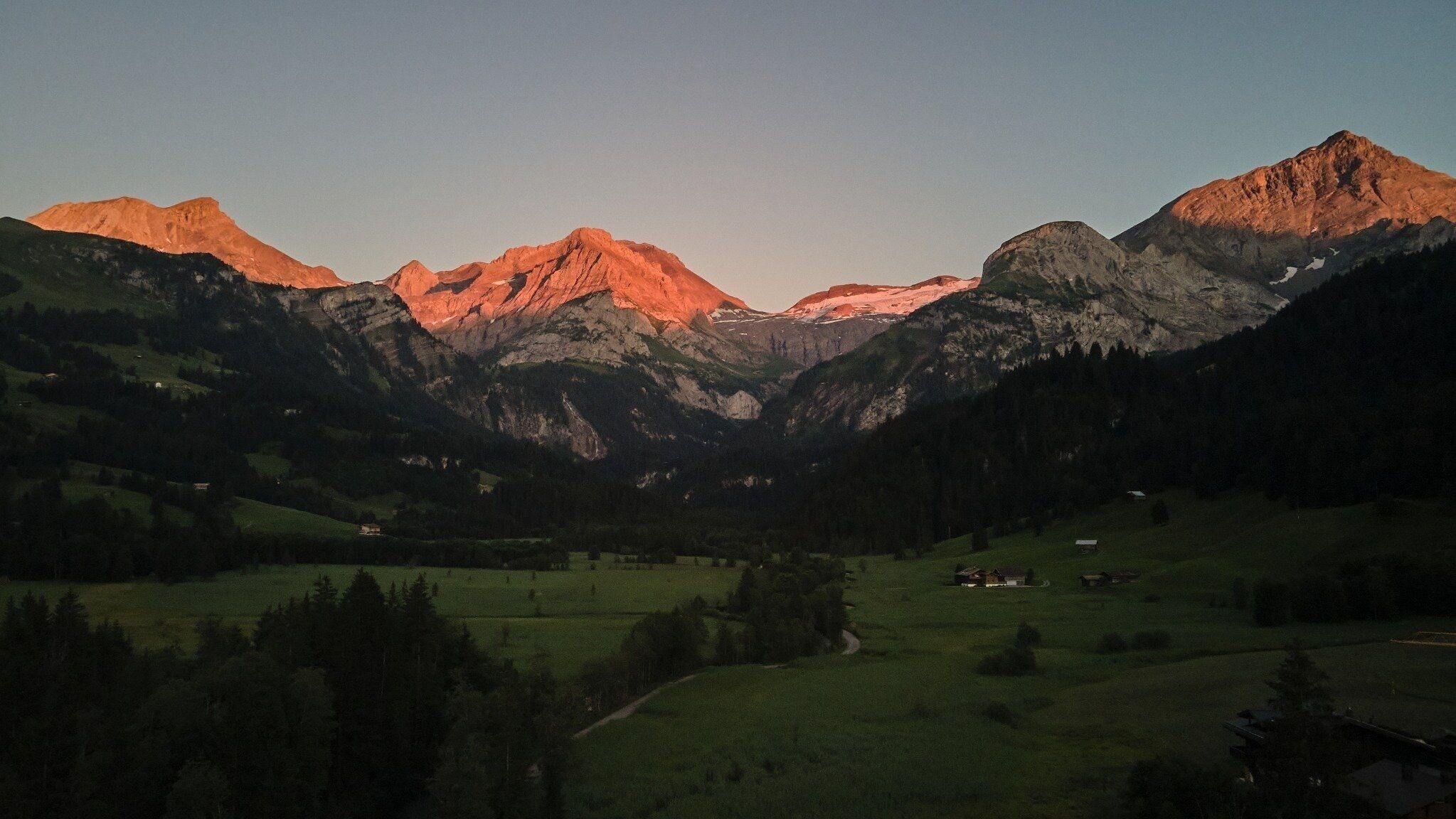 Un paysage montagneux avec une vallée, quelques maisons dispersées et un ciel dégagé.