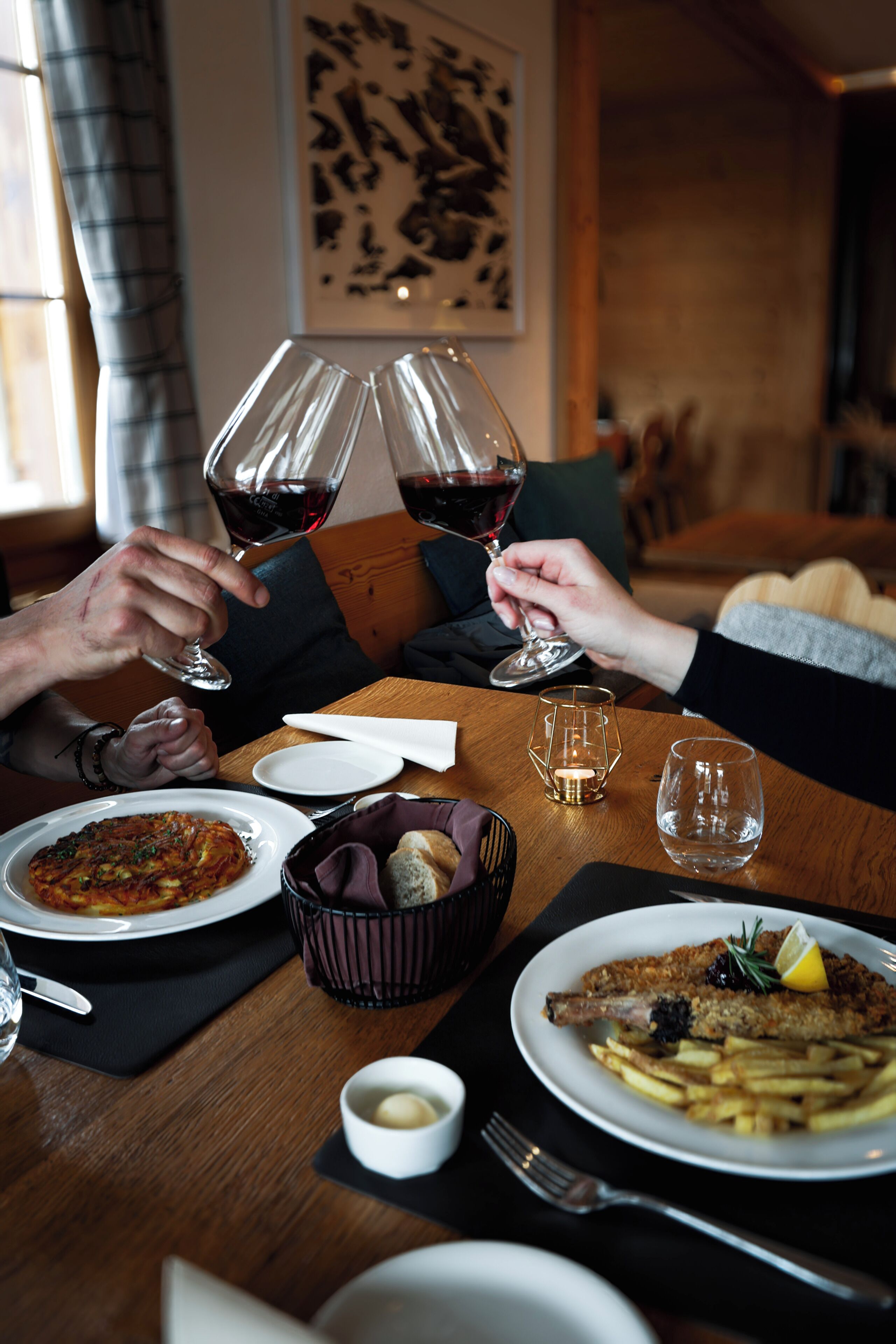 A dining table with plates of food, glasses of red wine, and a bowl of bread.