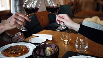A dining table with plates of food, glasses of red wine, and a bowl of bread.