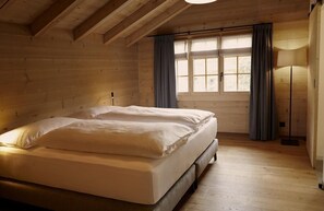 A wooden cabin bedroom with a bed, a window with curtains, and a floor lamp. - Hotel Alpenland (Lauenen)