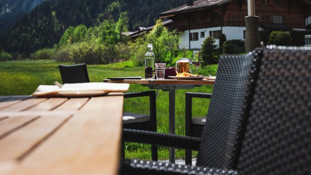 A table with a large umbrella, a chair, and a mountain view in the background. - Hotel Alpenland (Lauenen)