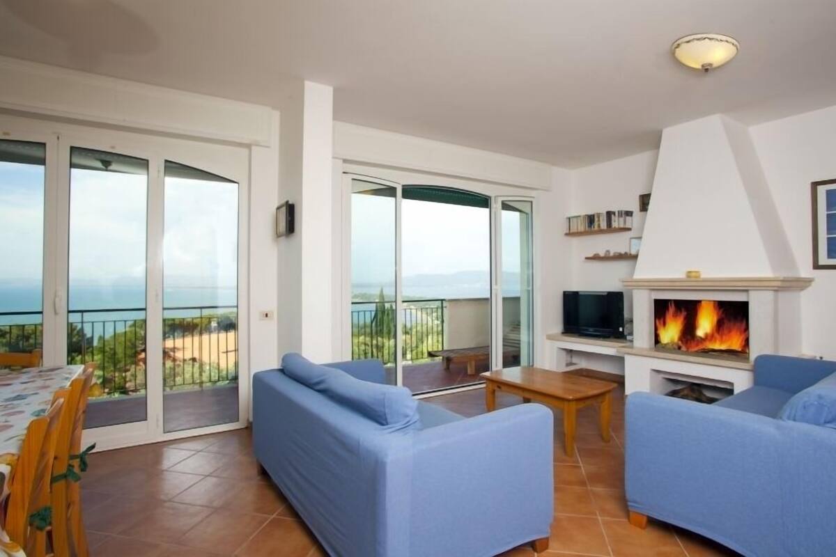 Ein Wohnzimmer mit Kamin, blauen Sofas, einem Fernseher und einem Balkon mit Aussicht.