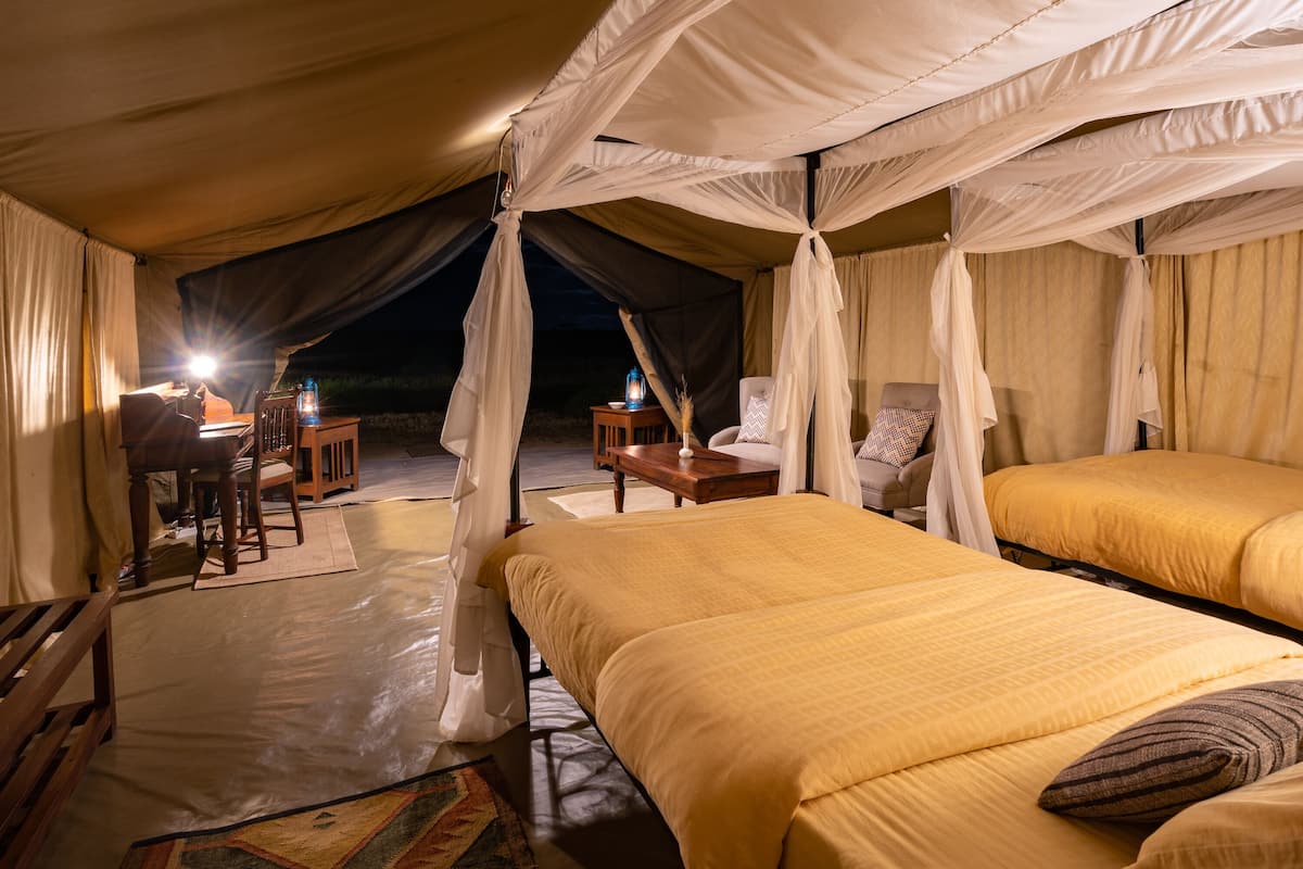 A tented accommodation with two beds, a dining area, and a table with a lantern.