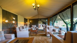 A tented accommodation area with multiple seating arrangements, including sofas and chairs, and a central table.