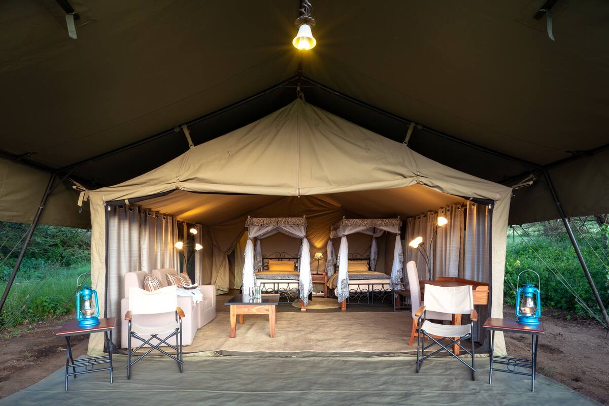 A tented accommodation with two beds, a sofa, a table, and two chairs.