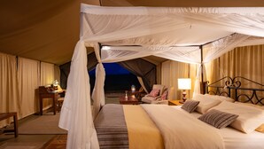 A tented room with a bed, a desk, a chair, and a lamp.