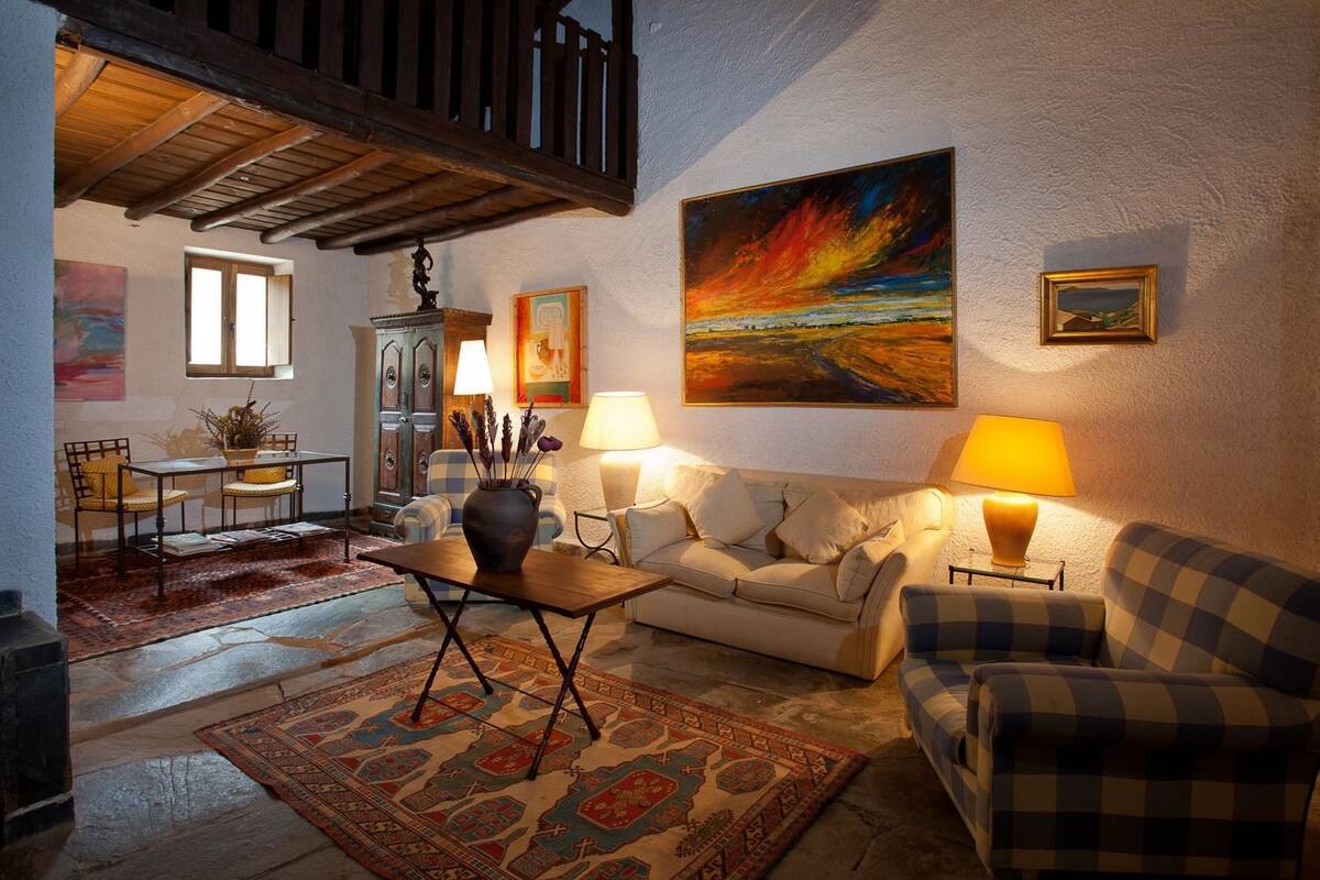 Een gezellige woonkamer met een bank, twee fauteuils, een salontafel en een open haard. Aan de muur hangt een groot schilderij en een raam zorgt voor natuurlijk licht.