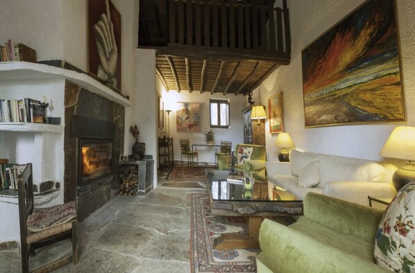 Una sala de estar acogedora con chimenea, un sillón verde, un sofá blanco y un cuadro en la pared.