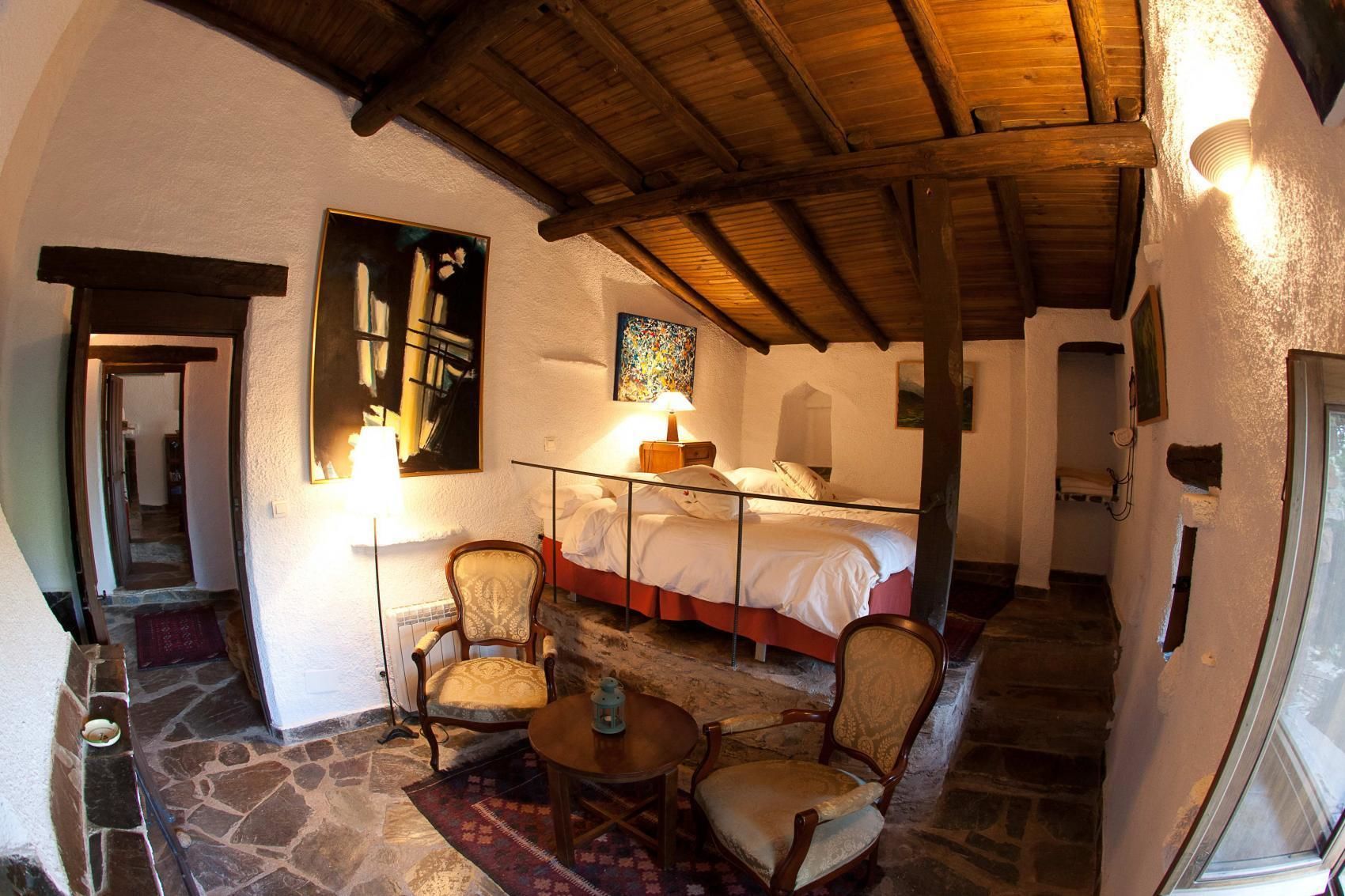 A cozy room with a bed, two chairs, a table, and a lamp.