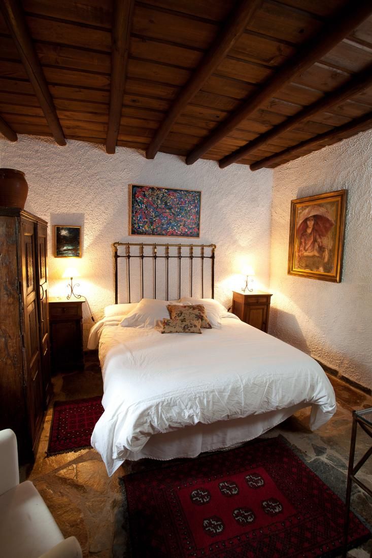 Ein Schlafzimmer mit Holzbalkendecke, einem Bett mit weißen Leinen, einem roten Teppich mit Muster und zwei Nachttischen mit Lampen.
