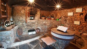 A stone-walled room with a wine cellar, featuring wine bottles, baskets, and a wooden bench.