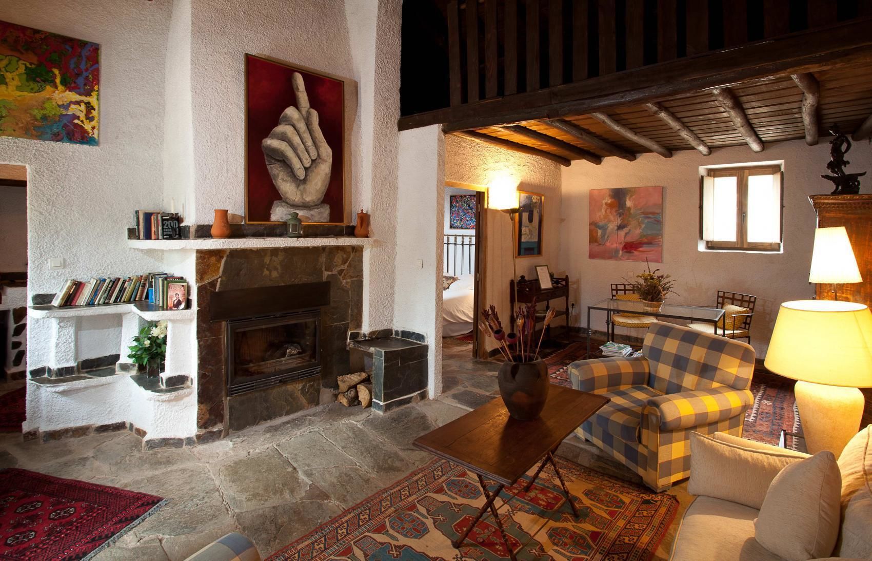 A cozy living room with a fireplace, bookshelves, a checkered sofa, and a dining area.