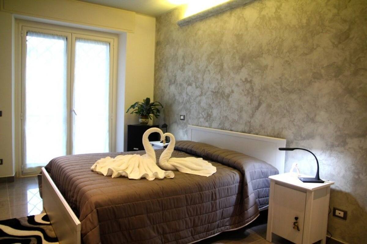 A bedroom with a large bed, a bedside table with a lamp, and a potted plant.