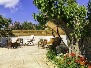 An outdoor patio with a table and chairs, a hanging chair, and a tree with a swing. - Pretty Spiti Holiday Home (Zakynthos)