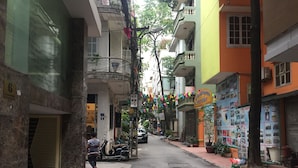 A narrow street lined with multi-story buildings, some with balconies and potted plants. - Granda Legend Apartment (Hanoi)